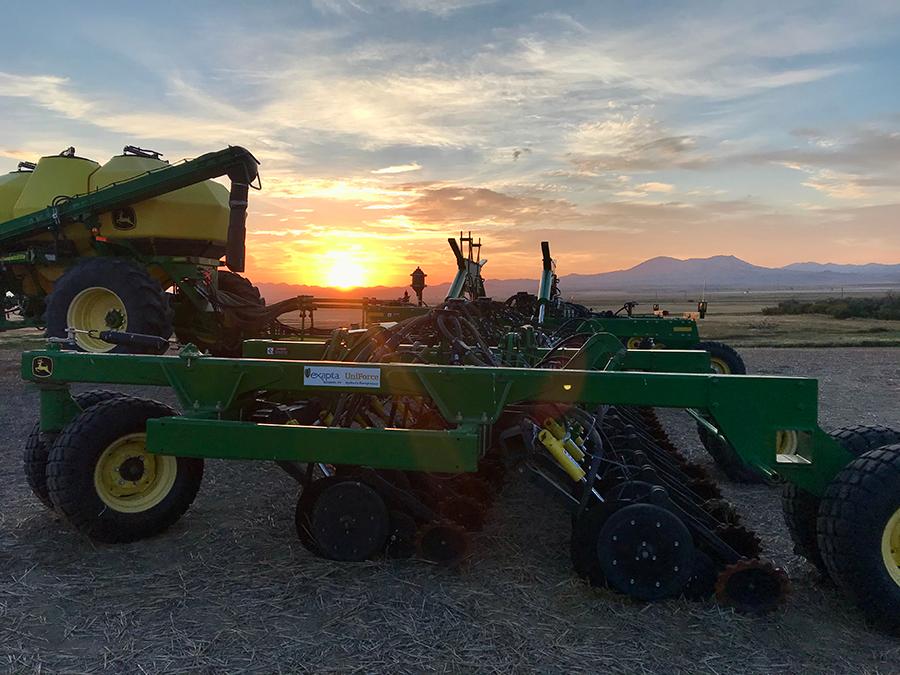 John Deere drill in a field with a sunset in the background.